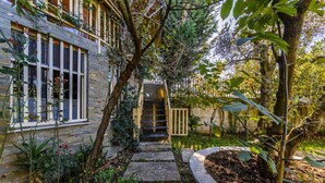 A stone pathway leading to a wooden gate, surrounded by lush greenery and a stone building with large windows. - Ferma Gold | Double Room by PikHost (Tiranë)