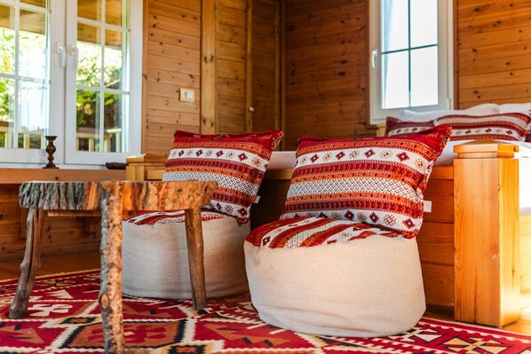 A cozy cabin interior with wooden walls, a bench, and two cushioned chairs with patterned pillows.