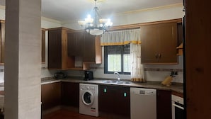 Une cuisine de taille réduite, dotée de meubles en bois, d’un lave-linge, d’un lave-vaisselle et d’une fenêtre avec des rideaux.