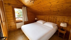 Een kamer met houten lambrisering, een bed, twee nachtkastjes, een raam met gordijnen en een deur.