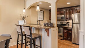 A kitchen with a central island, bar stools, a refrigerator, and wooden cabinets. - Beautiful Plaza Condo | 01 (Kansas City)