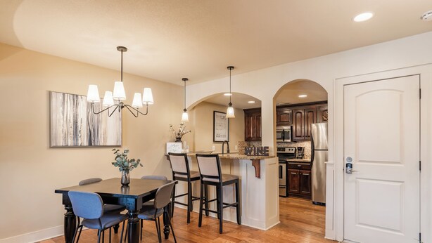 A dining area with a wooden table and chairs, a chandelier, and a kitchen in the background. - Beautiful Plaza Condo | 01 (Kansas City)