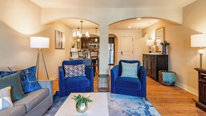 A spacious living room with two blue sofas, a coffee table with a plant, and a kitchen visible through an archway. - Beautiful Plaza Condo | 01 (Kansas City)