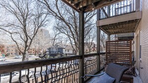 A balcony with a wooden bench and a table, overlooking a street with cars and buildings. - Beautiful Plaza Condo | 01 (Kansas City)