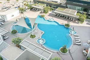 Vista aerea di un hotel moderno con una grande piscina centrale, lettini e una terrazza sul tetto.