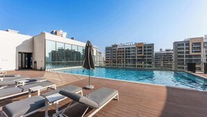 A rooftop swimming pool with lounge chairs and umbrellas, surrounded by modern buildings. - StayShort - Contemporary 1BR Meydan Sleeps 4 (Meydan)