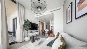 A modern living room with a sofa, a coffee table, and a potted plant. There is a dining area in the background with a table and chairs. - StayShort - Contemporary 1BR Meydan Sleeps 4 (Meydan)