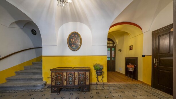 A staircase with a wooden handrail, a bench with a floral pattern, and a wall-mounted painting.