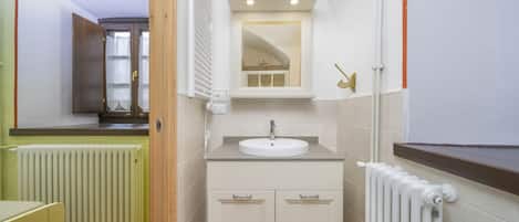 Une salle de bain avec un lavabo blanc, des meubles en bois, un miroir et un radiateur.
