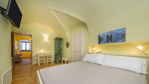 A bedroom with a bed, a desk, a chair, a wall-mounted TV, and a painting.