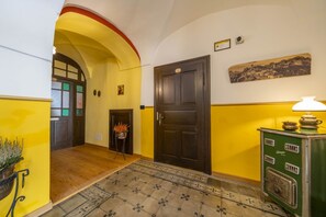A hallway with a wooden floor, a yellow wall, a dark wooden door, a green stove, and a small plant.