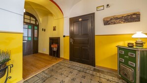 A hallway with a wooden floor, a yellow wall, a dark wooden door, a green stove, and a small plant.
