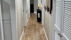 Un couloir avec un plancher en bois, des murs blancs et des portes fermées.
