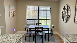 Un coin repas comprenant une table et des chaises, une fenêtre avec des stores et un élément décoratif en métal accroché au mur.