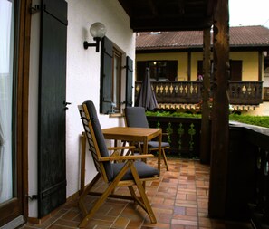 Un patio con una mesa de madera y dos sillas, un aplique en la pared y vistas a un edificio con balcón.