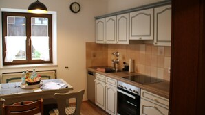 Une cuisine avec des meubles blancs, une cuisinière, un évier et une fenêtre avec des rideaux.
