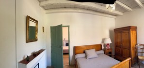 A bedroom with a bed, a wooden wardrobe, a nightstand with a lamp, a mirror, and a green door leading to another room. - Village house between sea and mountains (Pietrosella)