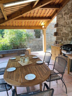 A wooden table with plates and a pitcher, surrounded by chairs, under a wooden roof structure. - Village house between sea and mountains (Pietrosella)