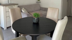 Een moderne eethoek met een ronde tafel, vier stoelen, een plant in pot, een lamp, een bank en een kast.