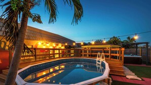 Una piscina esterna con un solarium in legno, una vasca idromassaggio e luci a tendina.