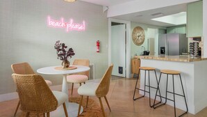 Una cucina moderna con un neon che recita 'beach please!' e sedie in vimini attorno a un piccolo tavolo da pranzo.