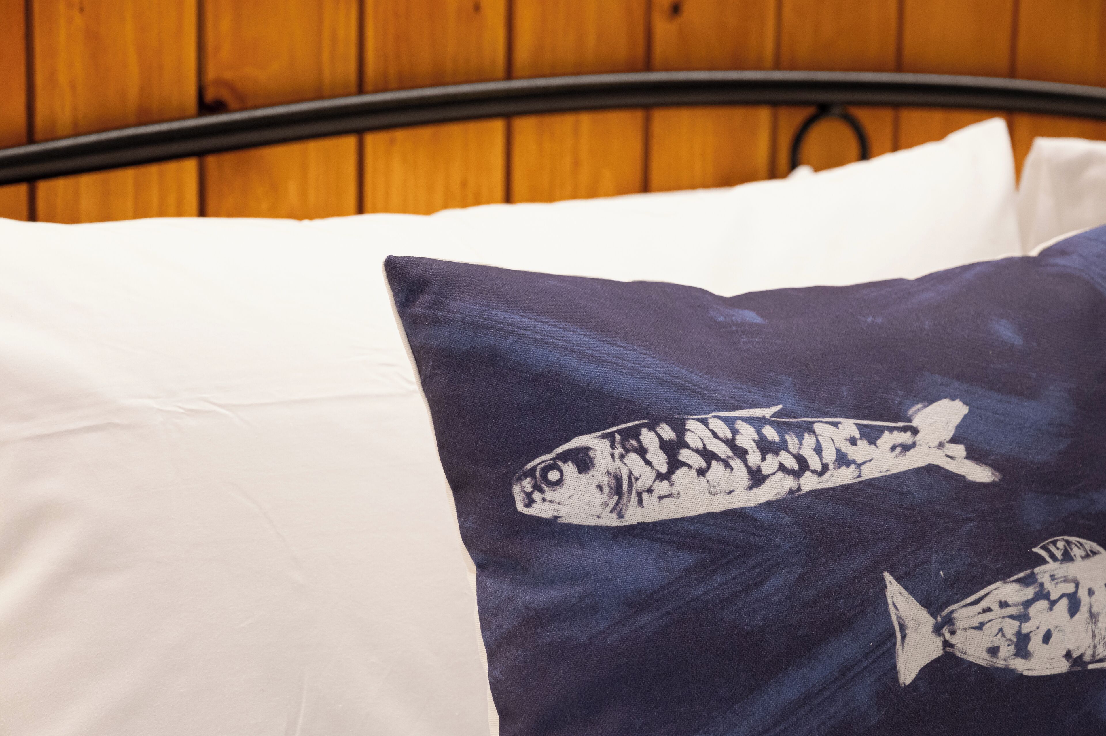 Ein Bett mit einem weißen und einem dunkelblauen Kopfkissen mit Fischmotiven.