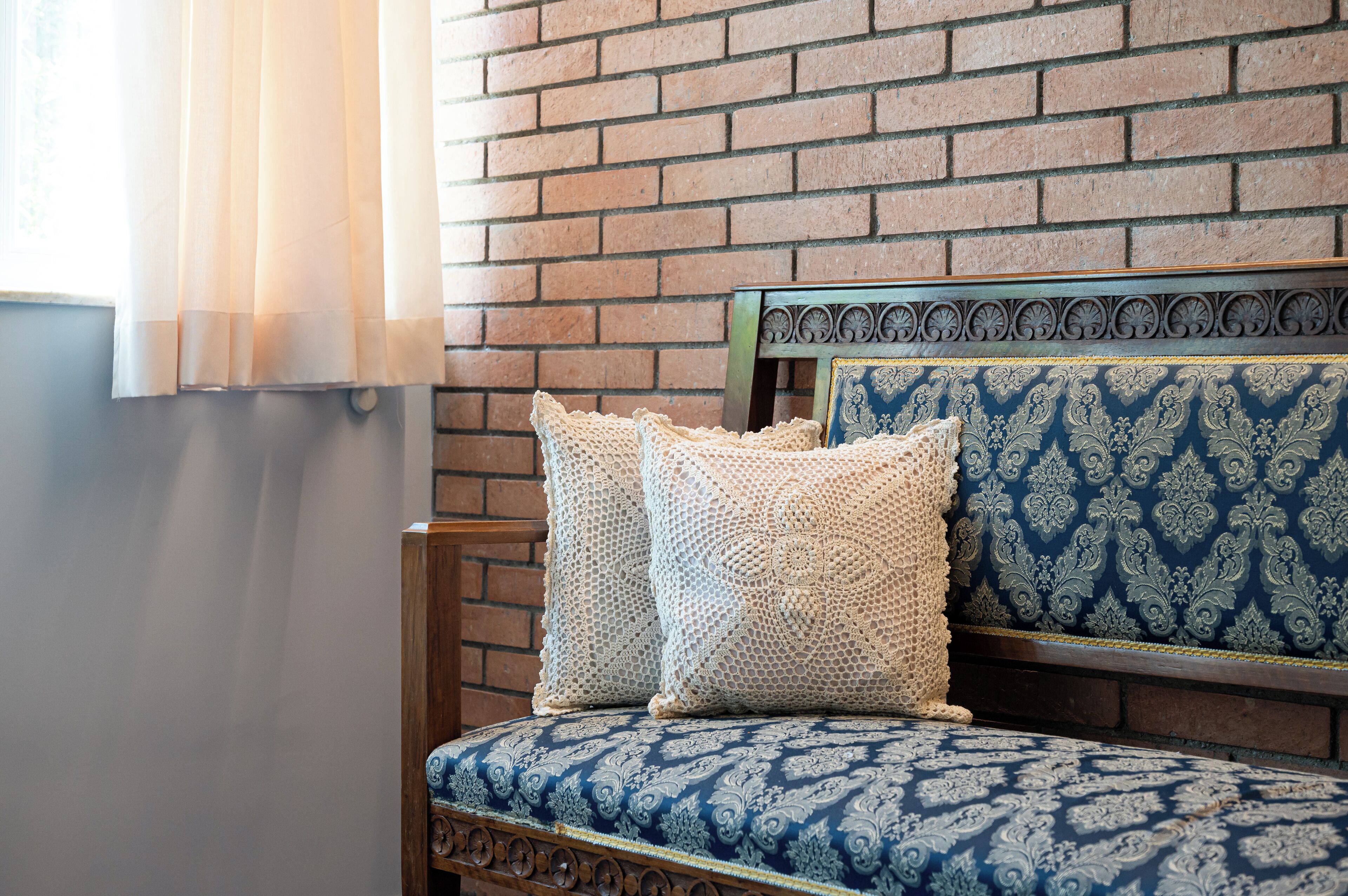 A wooden bench with a patterned cushion and a decorative headboard against a brick wall.
