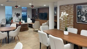 Een moderne hotel lobby met een groot houten receptiebalie, witte leren stoelen en een televisie.
