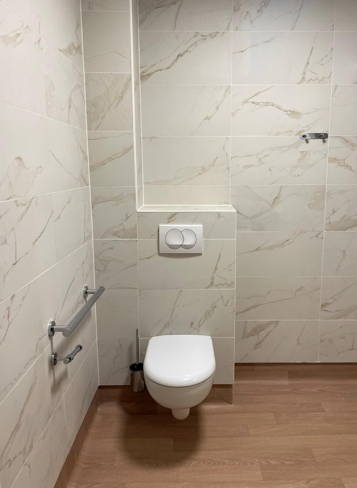 Baño con inodoro, barras de apoyo y secador de manos.