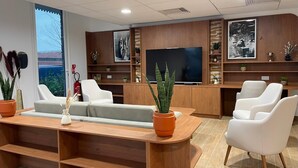 Een modern kantoor met een groot bureau, witte stoelen, een bank en een televisie aan een houten wand.