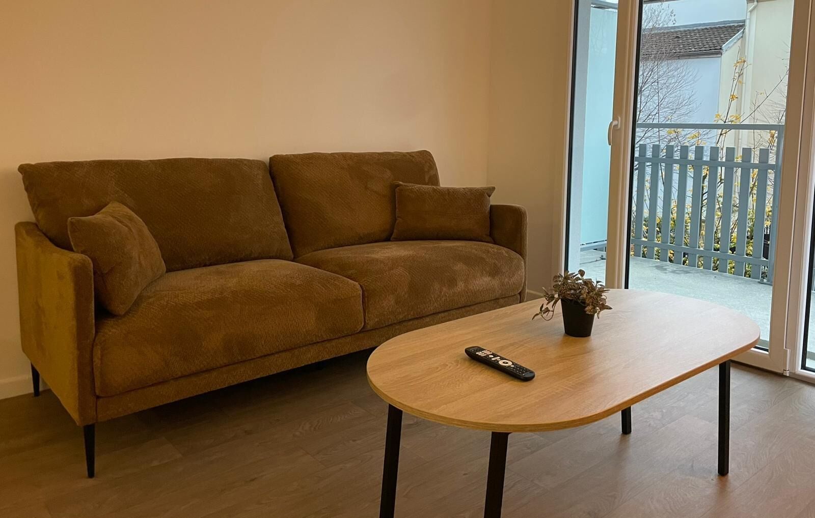 Een bruine bank met een afstandsbediening en een potplant op een houten tafel.