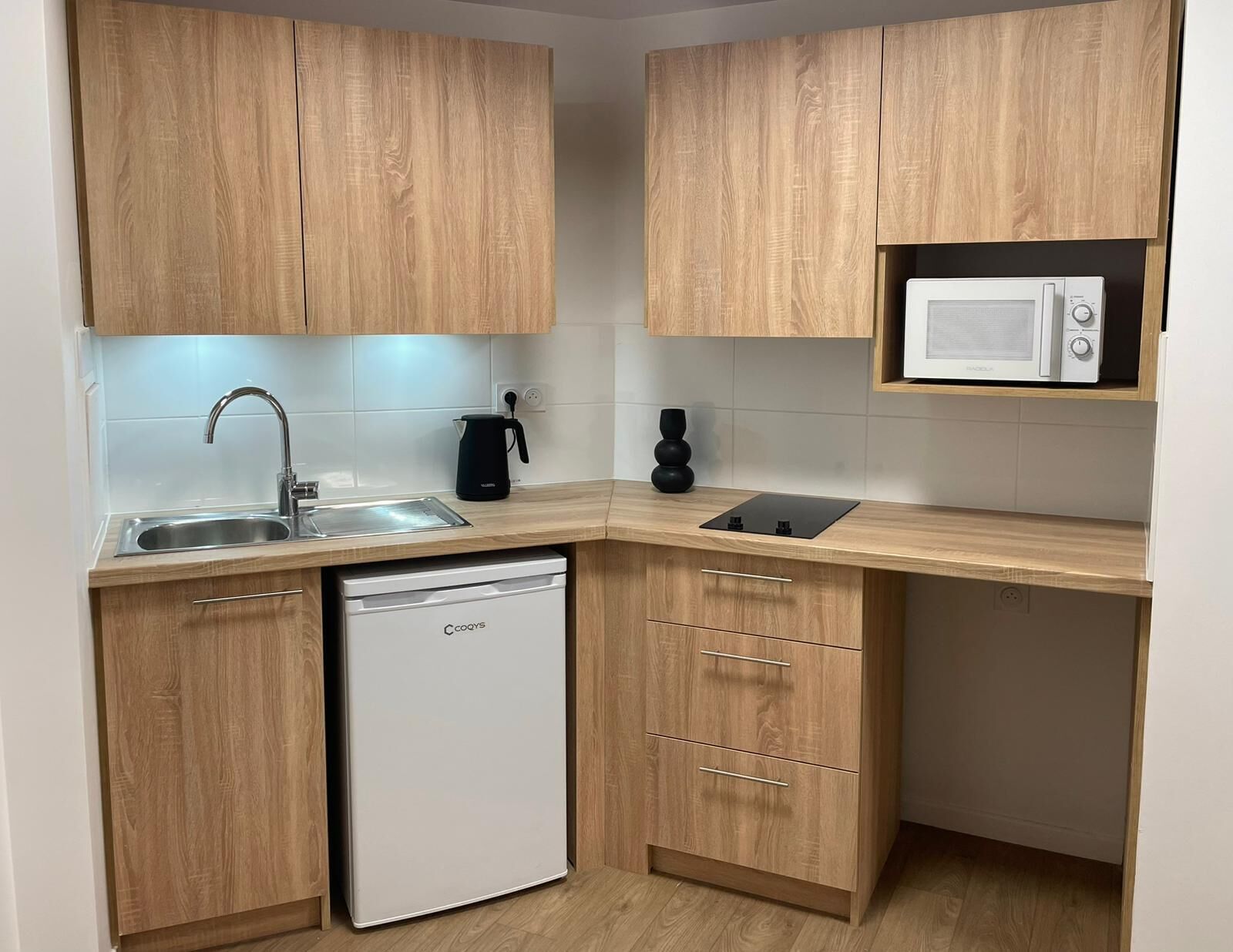 A compact kitchen with wooden cabinets, a built-in microwave, a sink, and a dishwasher.