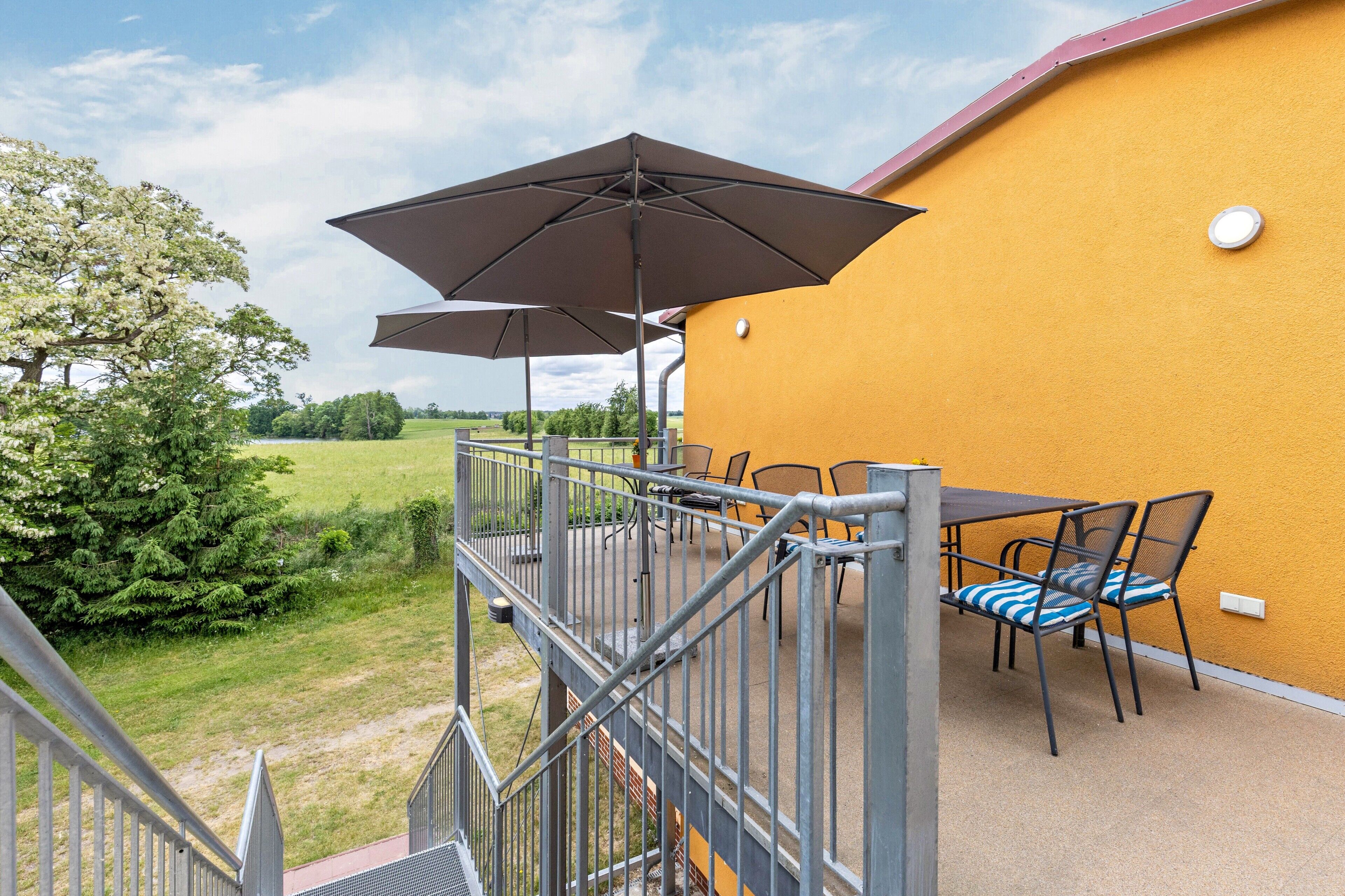 Een balkon met tuinmeubilair, waaronder een tafel en stoelen, en twee parasols.