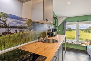 A modern kitchen with a wooden countertop, stainless steel sink, and a view of a green field through a large window.
