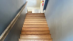 Una escalera de madera con barandilla a la izquierda, que conduce a un rellano con una puerta arriba.