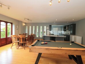 A pool table in a room with a dining area, kitchen, and large windows. - Lady Of Lourdes (Ross-on-Wye)