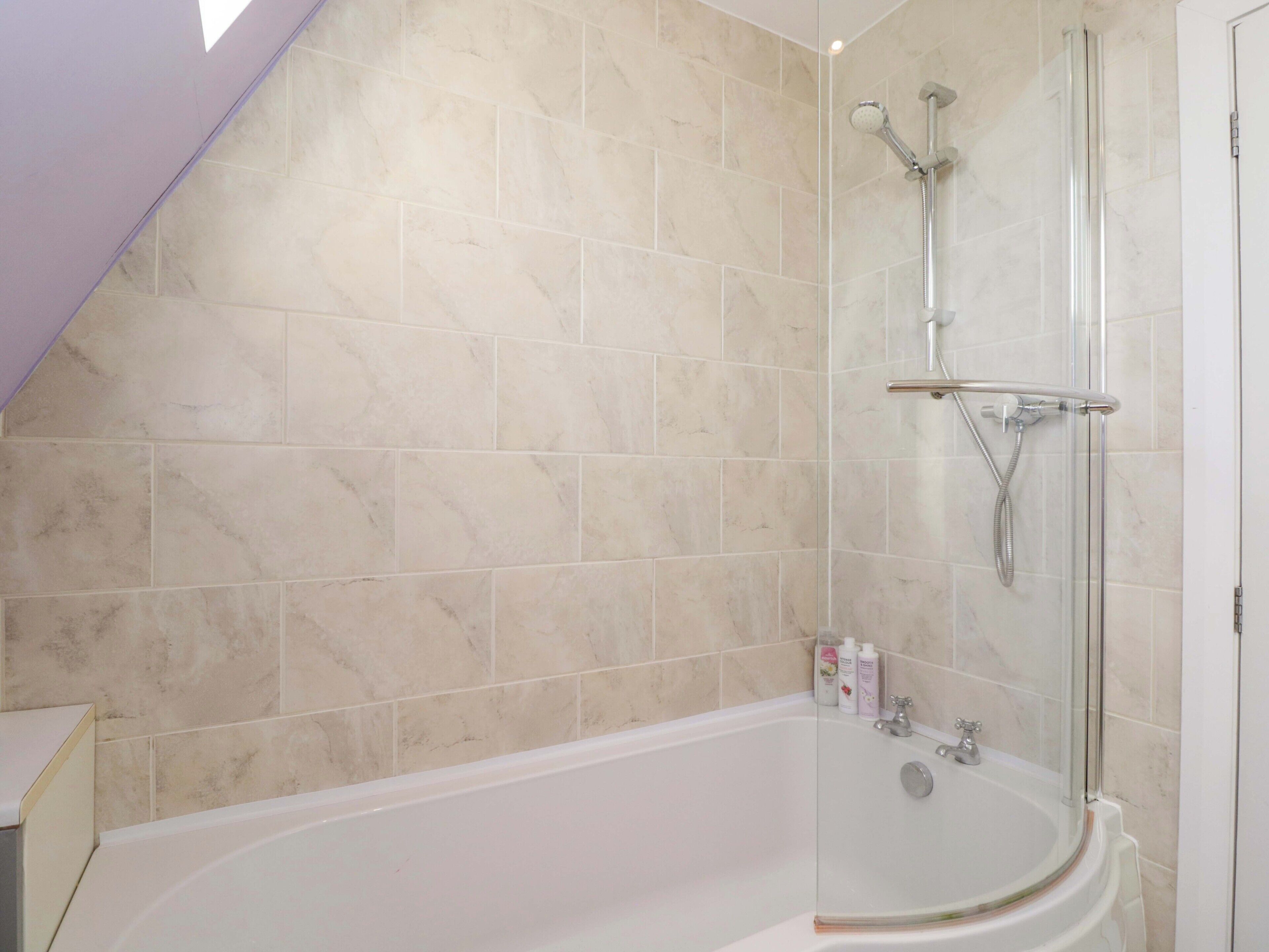 A bathroom with a bathtub, a glass-enclosed shower, and beige marble tiles.