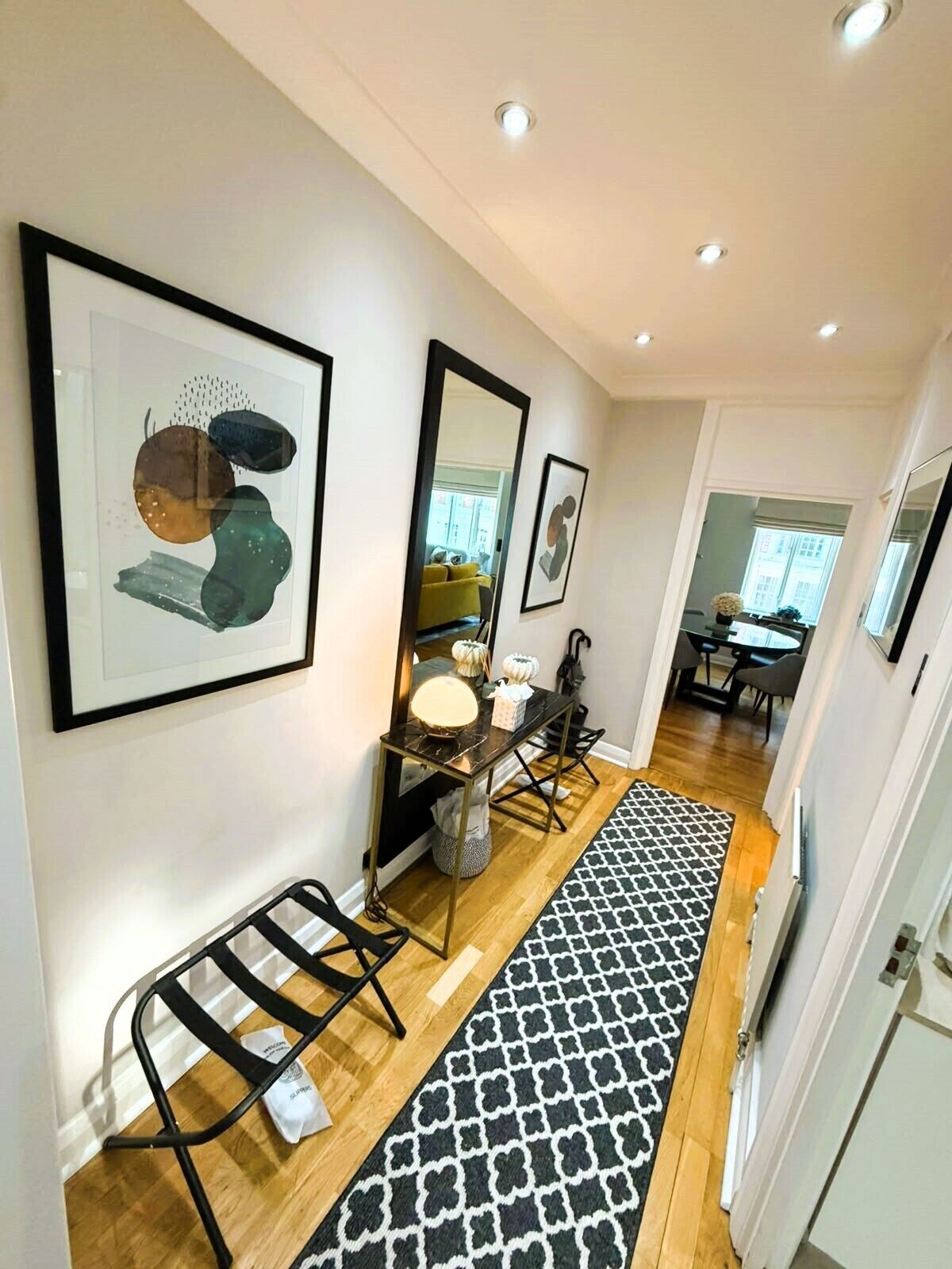 A hallway with a black and white patterned rug, a black metal bench, and framed artwork on the walls.