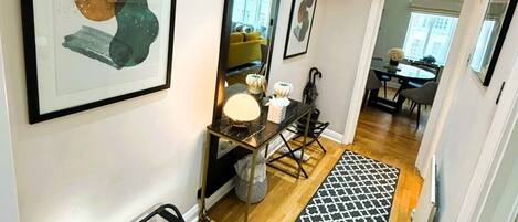 A hallway with a black and white patterned rug, a black metal bench, and framed artwork on the walls.