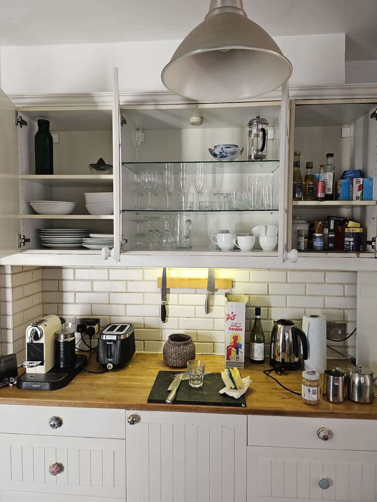 A kitchen with a wooden countertop, a coffee machine, a toaster, a kettle, and a hanging knife rack.