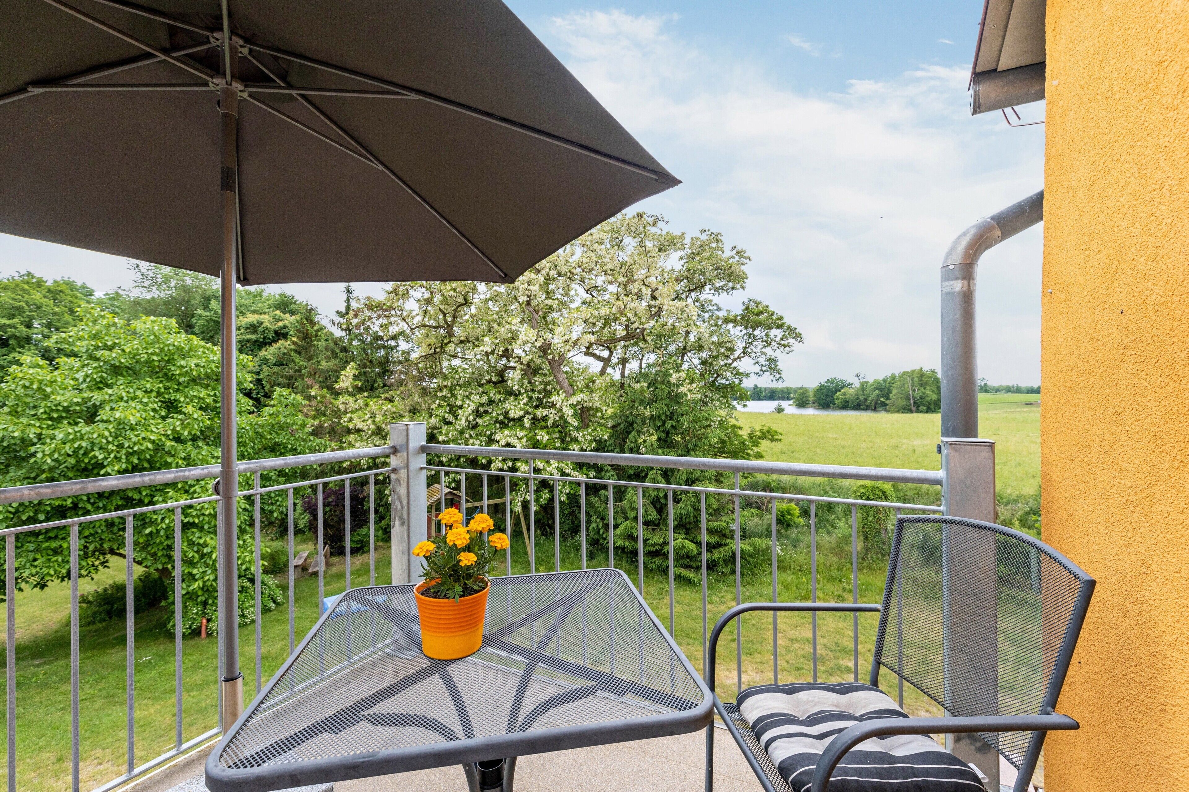 Un balcon avec une table, une chaise et un pot de fleurs, donnant sur un paysage verdoyant.