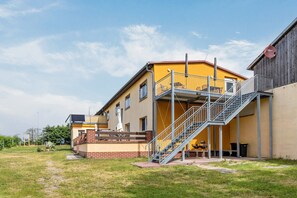 Kaksikerroksinen rakennus, jossa on parveke, ulkotila istumista varten ja portaikko, joka johtaa ylempään kerrokseen.
