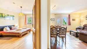 A room with a bed, a sofa, a dining table with chairs, and a lamp.