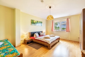 Ein Schlafzimmer mit Bett, Nachttisch, Lampe, Fenster mit Vorhängen und einem Bild an der Wand.