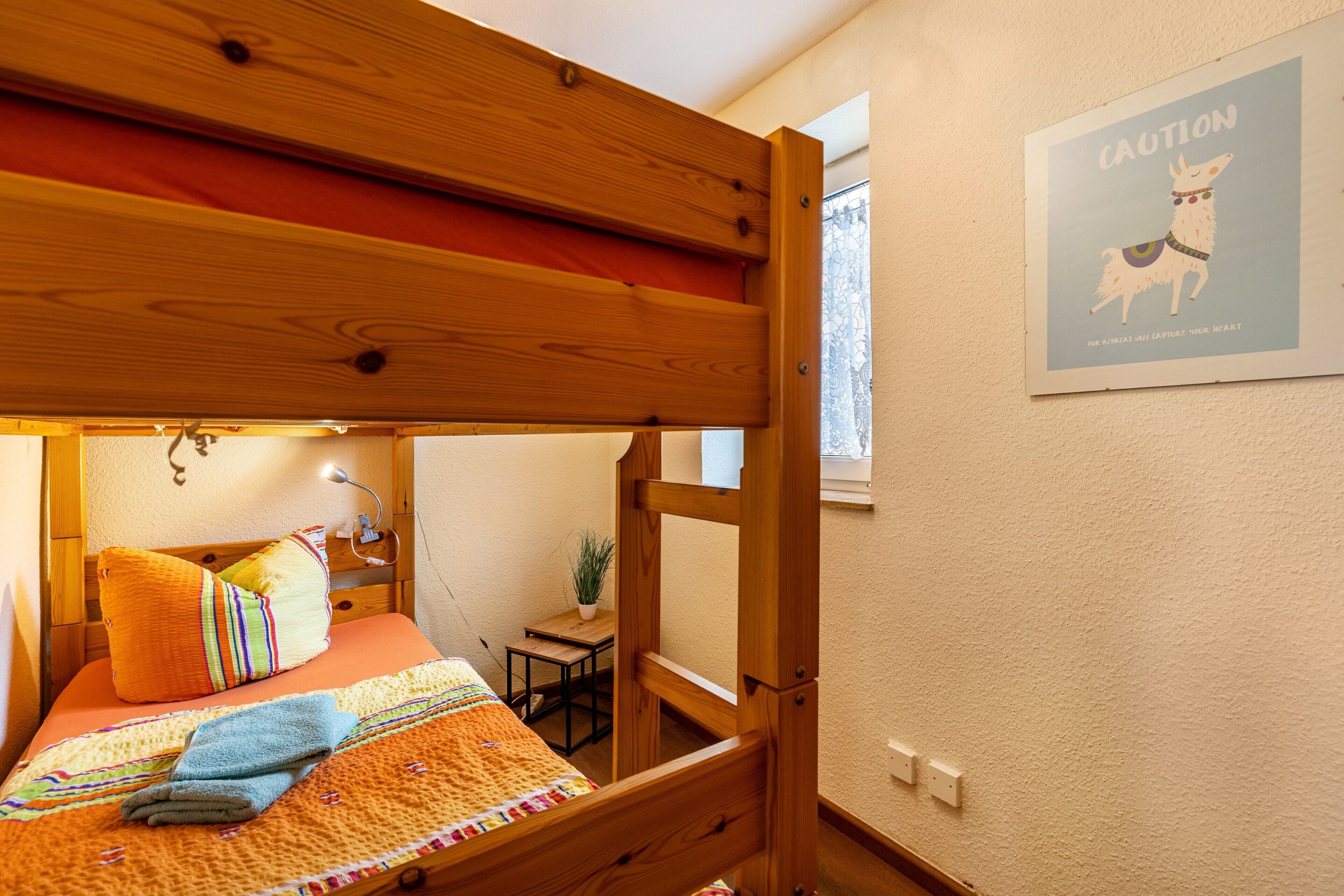 A bunk bed with a wooden headboard, a small table with a plant, and a framed poster on the wall.