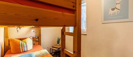 A bunk bed with a wooden headboard, a small table with a plant, and a framed poster on the wall.