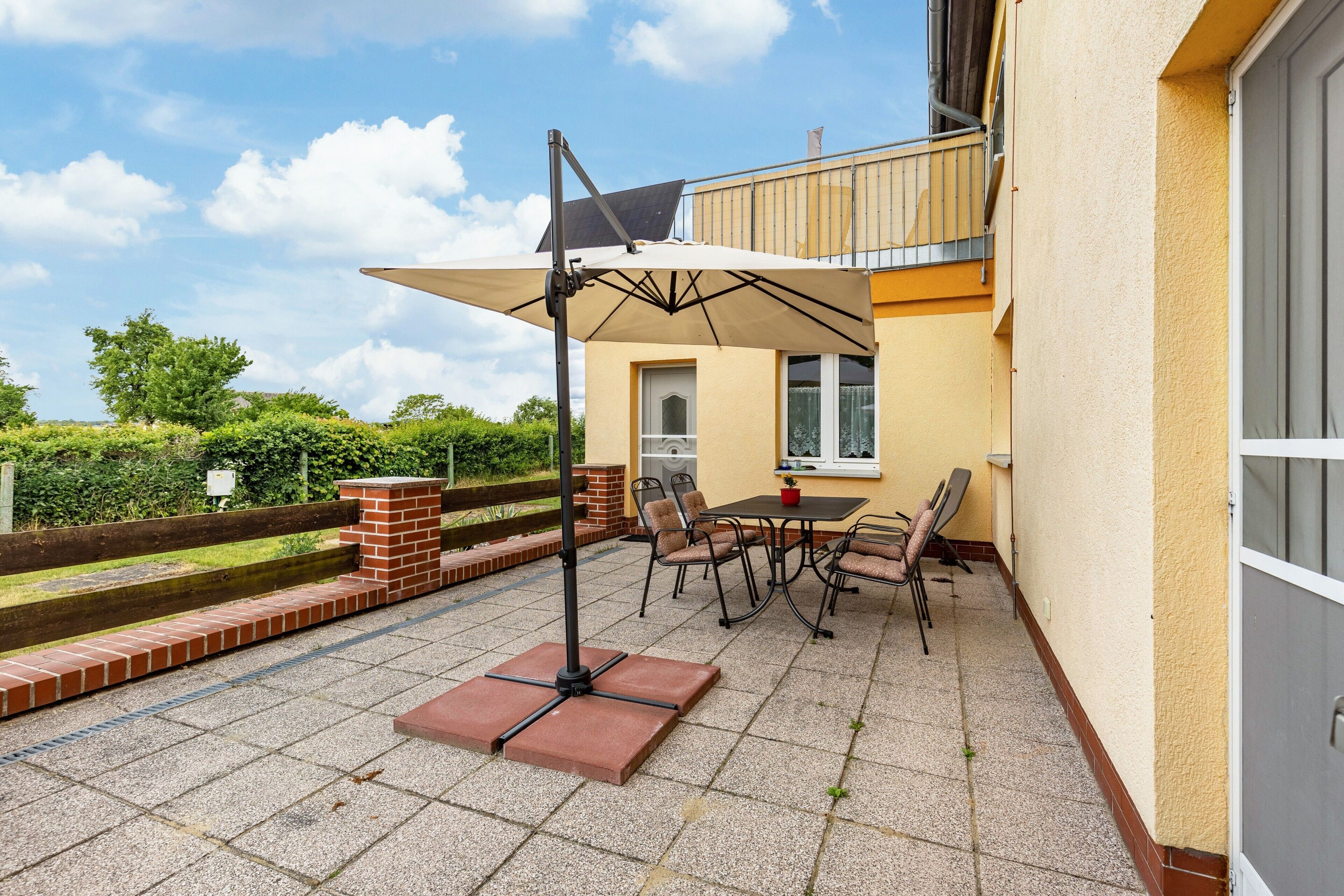 Une terrasse extérieure avec une table et des chaises, un parasol solaire et un jardinier en briques.