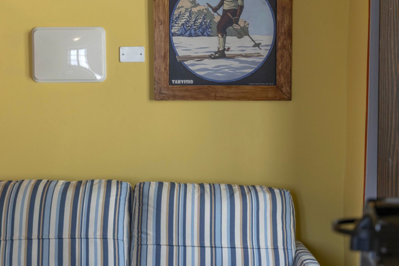 Een kamer met een gele muur, een lijst met een skiënd persoon, een wit paneel en een gestreepte bank.