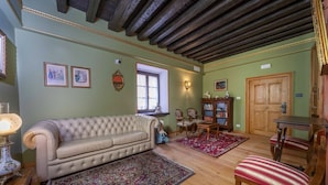 A room with a tufted sofa, a wooden table, a patterned rug, and a wooden door. - GuestHost - A welcoming apartment of approximately 50 square meters, perfect for five people, located on the first floor of a historic building built in 1864 and renovated in 2025 while maintaining its historic atmosphere (NO elevator).The property is lo (Tarvisio)