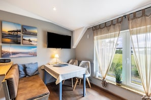 Een kamer met een flatscreen televisie, een bank, een eettafel en een raam met gordijnen.